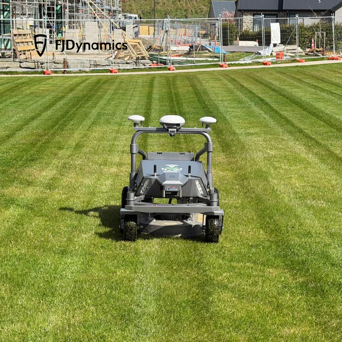 FJDynamics robotic lawn mower operating on a well-maintained grass field with construction site in the background